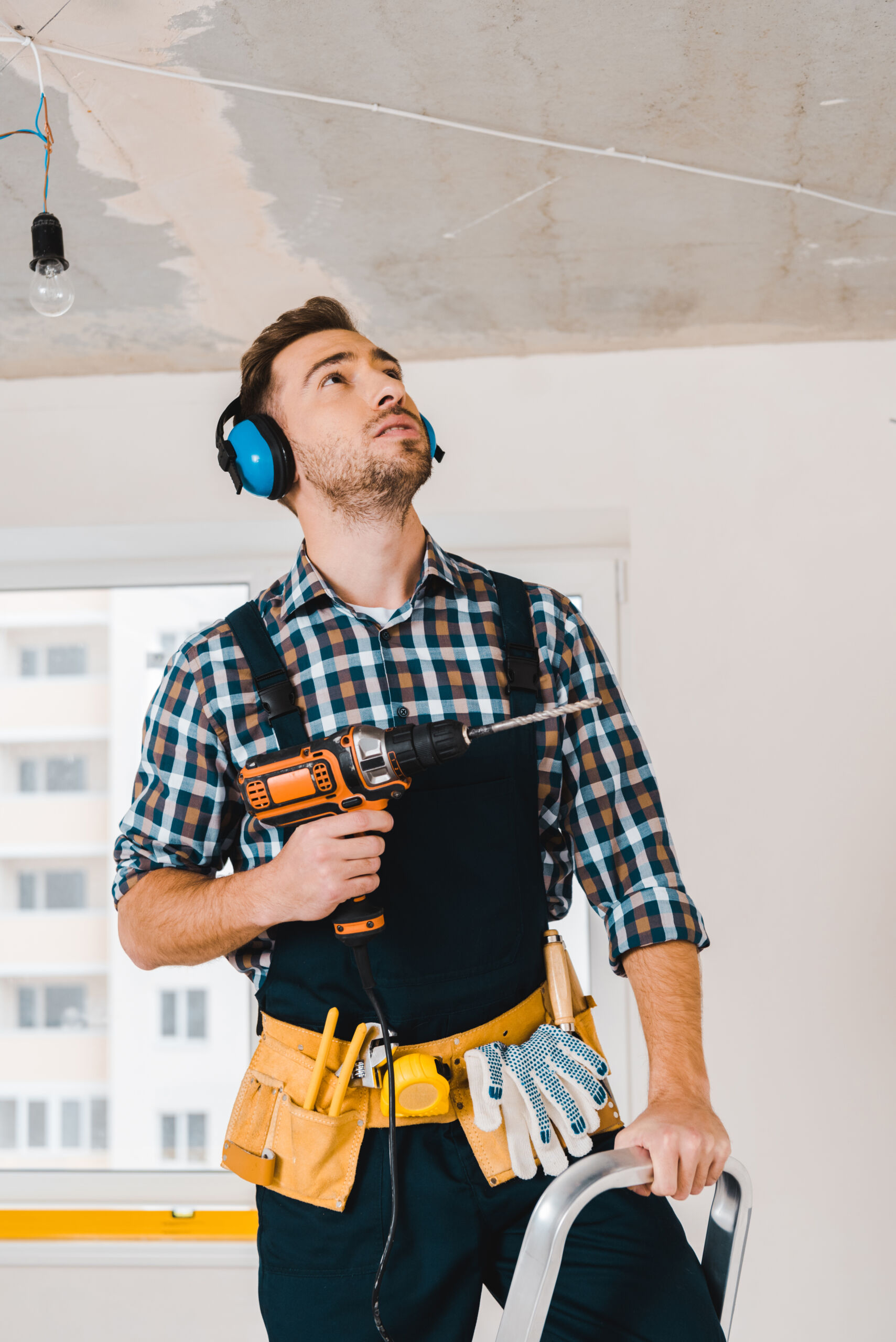handsome handyman holding drill in hand and looking on ceiling